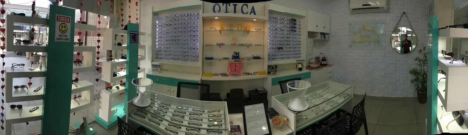 Vista panorâmica da loja com expositores, balcões de vidro e parede de armações